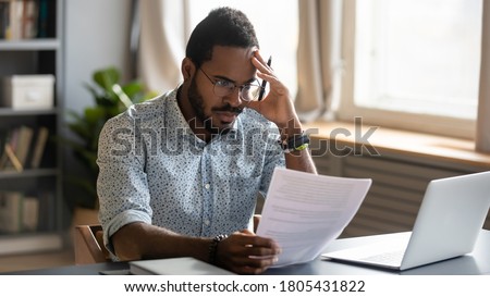 Stressed dissatisfied African American businessman reading letter with bad news, unexpected debt, bank or job dismiss notification, student working on difficult project, holding document in hand Royalty-Free Stock Photo #1805431822