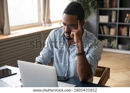 Thoughtful doubtful African American businessman looking at laptop screen, pondering online project plan or strategy, solving problems, student working on difficult task, doing homework Royalty-Free Stock Photo #1805431852