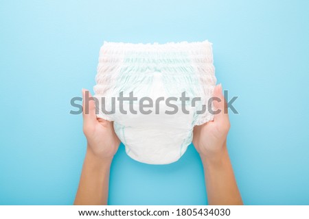 Young mother hands holding white baby diaper pants on light blue table background. Pastel color. Closeup. Point of view shot. Royalty-Free Stock Photo #1805434030