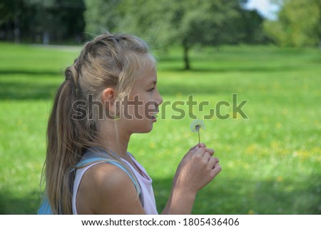 Eight-year-old girl on a green background of a Park holding a dandelion and making a wish, Russia.