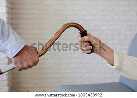 Mature female in elderly care facility gets help from hospital personnel nurse. Close up of aged wrinkled hands of senior woman reaching to male doctor handing her a quad cane. Copy space, background.