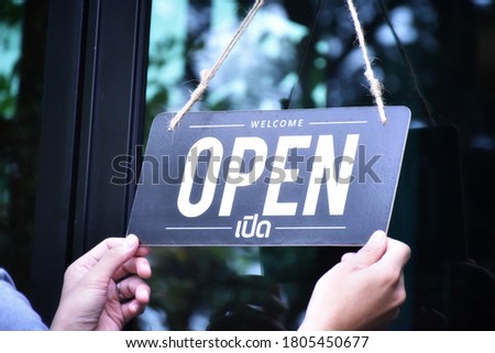 Shop owner is hanging 'Open' label on glass windows to open the shop and welcome customers. Thai language in the picture means 'Open' in English.