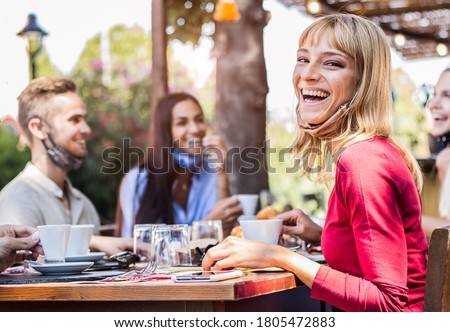 Happy young woman wearing face mask smiling at the camera at the restaurant cafè. Group of friends drinking coffee sitting at the bar. Royalty-Free Stock Photo #1805472883