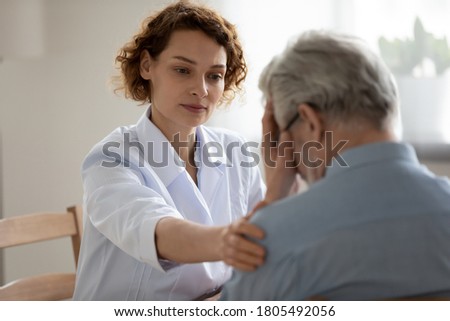 Caring young woman doctor comforting depressed unhealthy mature patient at meeting in hospital, therapist physician gp caregiver touching senior man shoulder, expressing empathy and support Royalty-Free Stock Photo #1805492056