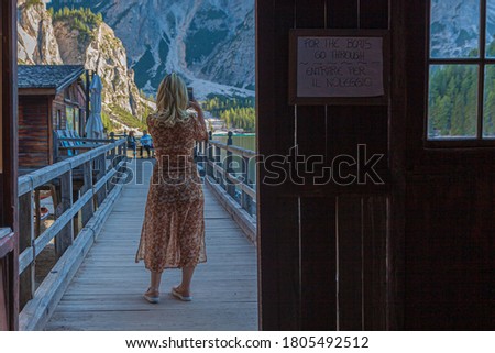 Blonde girl shot back to back takes a picture from the jetty of Lake Braies, South Tyrol, Italy
