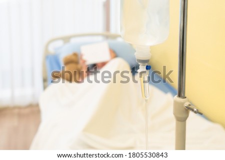 young asian girl is lying in the hospital bed and watching cartoon in tablet. healthcare and medical concept (focus at intravenous fluid)