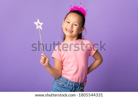 Little Princess Concept. Little Asian Kid Wearing Crown Holding Magic Stick Smiling To Camera Over Purple Studio Wall Royalty-Free Stock Photo #1805544331