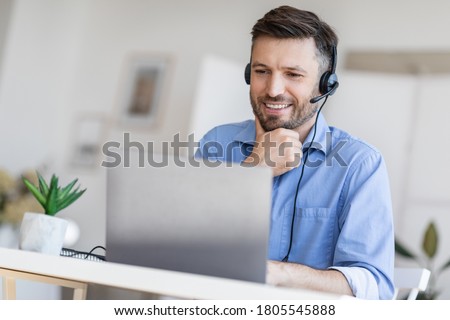 Hotline Support Service. Handsome male call center operator in headset working with laptop in modern office, looking at computer screen, free space Royalty-Free Stock Photo #1805545888