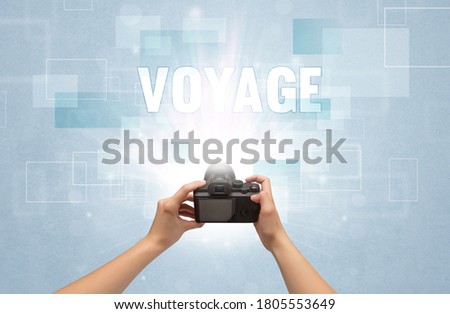 Close-up of a hand holding digital camera with VOYAGE inscription, traveling concept