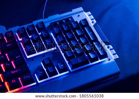 Gamer keyboard with blue backlight and red background light, modern laptop computer.