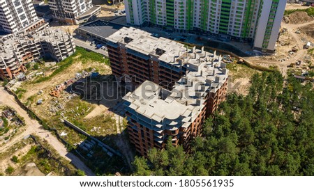 Shot of construction process of skyscraper structure. Aerial top-down photo of multi-story modern apartment building. Construction of urban buildings between green trees.