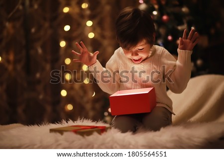 Family on Christmas eve at fireplace. Kids opening Xmas presents. Children under Christmas tree with gift boxes. Decorated living room with traditional fire place. Cozy warm winter evening home.