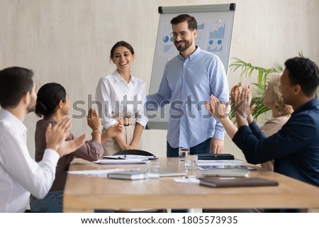 Smiling male leader praising happy millennial arab colleague at group meeting. Smiling diverse coworkers applauding, supporting new worker or congratulating with personal professional achievement. Royalty-Free Stock Photo #1805573935