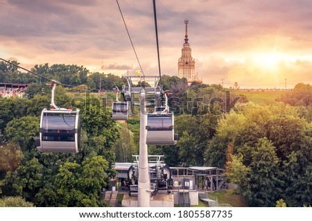 Cable car on Sparrow Hills at sunset, Moscow, Russia. Cableway cabins move over park, main building of Moscow State University in distance. Beautiful sunny urban landscape of Moscow in summer. Royalty-Free Stock Photo #1805587735