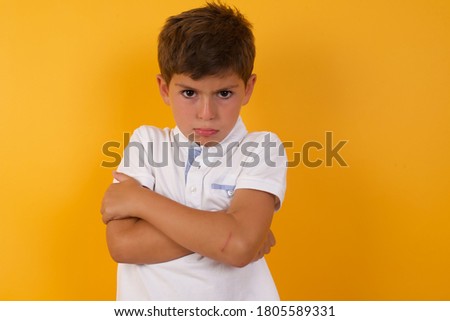 Picture of angry young handsome little boy crossing arms standing isolated over yellow background. Looking at camera with disappointed expression.