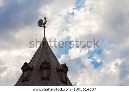 Roof of an old building with a rooster on top against a cloudy sky