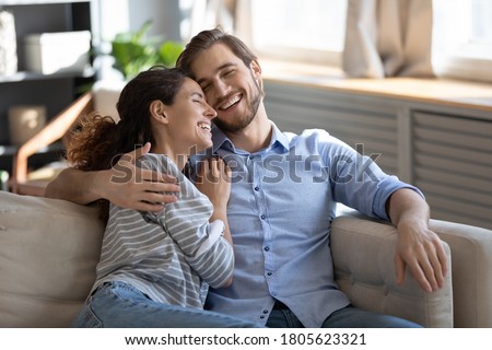 Emotional positive romantic family couple laughing at funny joke, relaxing together on sofa indoors. Happy young pretty woman enjoying communicating with beloved man at home dating, relations concept. Royalty-Free Stock Photo #1805623321