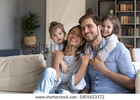 Loving small baby girls embracing smiling parents, looking away. Bonding affectionate young married couple enjoying spending holiday weekend free leisure time with two cute daughters, watching tv. Royalty-Free Stock Photo #1805623372