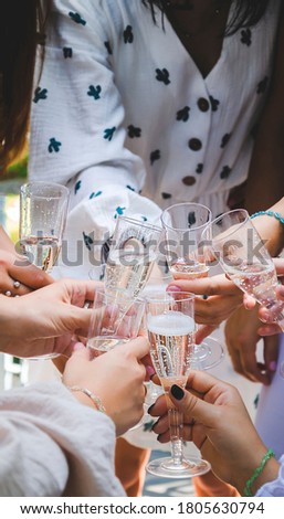 Close up picture of glasses with champagne on bachelorette party. Girls hands clinking glasses of drinks on the hen party. Bride to be and happiness of bridesmaids outside on the nature. 