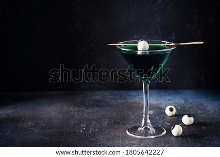Halloween coctail black widow with green drinks with eyes in glass on dark background, copy space, 
