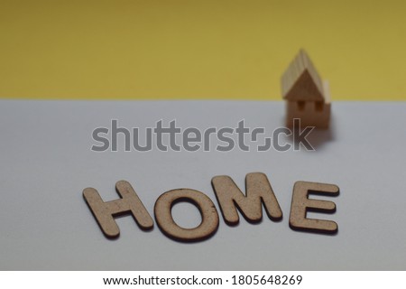 The word says HOME written in 3d wooden alphabet letters laid on a pair of solid color background with an incomplete house model. Conceptual image of broken family home, selective focus on letters.