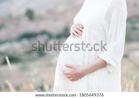 Pregnant woman wearing dress posing outdoors over nature background. Motherhood. Maternity. Healthy lifestyle.