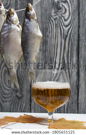 Dried river fish hangs on a rope. Nearby there is a glass of beer, dried maple leaves lie.