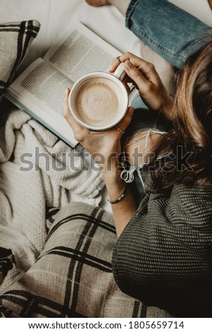 A girl reading a book and drinking coffee in the white bed with pillows. Vertical no face image