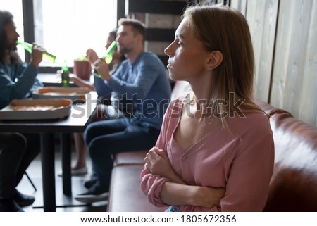 Upset offended young woman sitting separately, apart from diverse friends in cafe close up, sad excluded female feeling outsider, bad friendship concept, problem with communication, social outcast Royalty-Free Stock Photo #1805672356