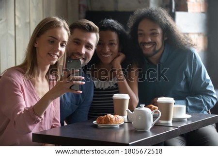 Happy diverse people taking selfie for social network, sitting at table in cafe, smiling young woman holding smartphone, photographing, posing for photo with friends, vlogger recording video
