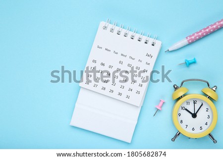 Calendar page with alarm clock and pen on blue background