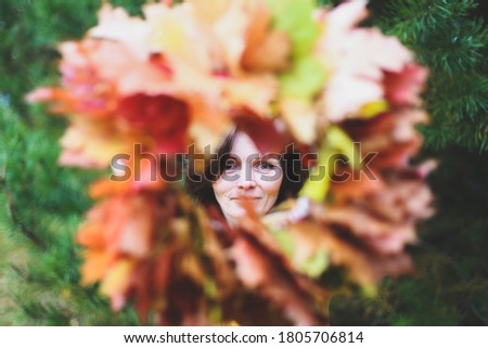 Brunette caucasian happy woman in circle frame of maple leaves wreath. Autumn harvest, nature concept. Flowers bouquet of orange, red, yellow leaves. Park, garden, forest fall photo shoot.