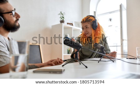 Female blogger, woman in headphones pointing at man while talking, recording conversation, interview with him for video blog. Content creator, filming, blogging. Focus on woman. Web Banner