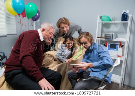 A family checking out pictures on the boy's phone, while they are visiting his sister at the hospital.