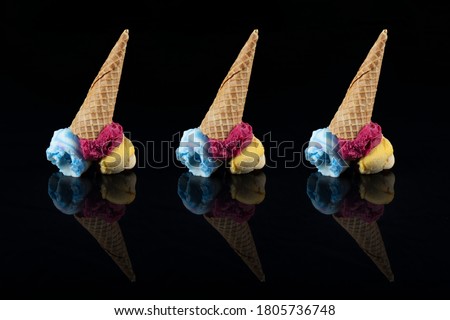 Fruit ice cream scoops overhead on a cornet, served with several colorful spoons isolated on black background.