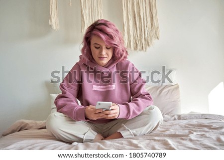 Hipster woman with pink hair holding smart phone chatting in social media, watching video content, texting messages, playing games, using mobile apps, surfing internet sit in bed at home. Vertical Royalty-Free Stock Photo #1805740789