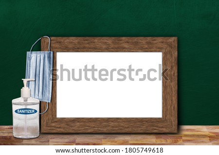 COVID-19 new normal education back to school concept in the classroom setting showing picture frame on chalkboard with copy space and face mask, hand sanitizer on wooden table.