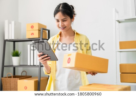 Startup small business, A young Asian woman checking online order on digital tablet and packing boxes for products to send to customers. working at the home office. Royalty-Free Stock Photo #1805800960