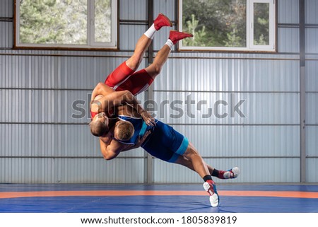The concept of fair wrestling. Two greco-roman  wrestlers in red and blue uniform wrestling   on a wrestling carpet in the gym. Royalty-Free Stock Photo #1805839819
