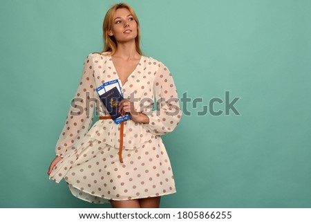 Joyful young woman in polka dot dress is holding airline tickets with a passport on a blue background. Rejoices in the resumption of tourism after the coronovirus pandemic.