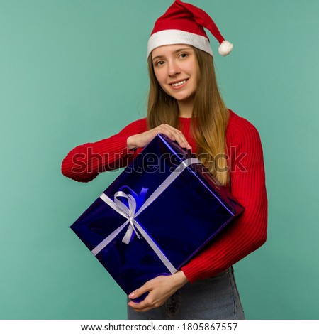Happy excited young woman in santa claus hat with gift box over blue background - image