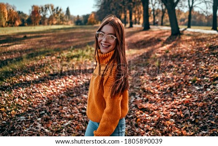 Young woman in park in autumn. Teenager enjoying good weather with yellow leaves on fall nature background.