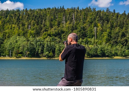 Adult man in hoodie walking around lake with DSLR camera ans shooting, beautiful summer day, half body portrait, landscape photography concept
