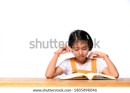 Asian female kid who wear glasses while concentrate reading a textbook on table on white background in studio. Learning of Schoolgirl. Memorize, learning by heart concept. Royalty-Free Stock Photo #1805898046