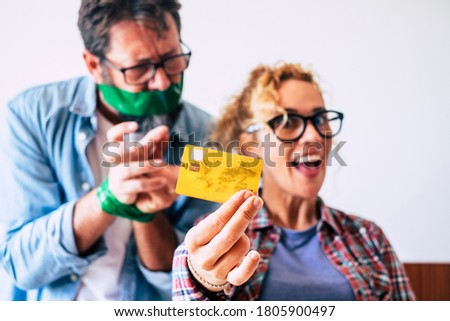 Credit card and shopping economy business concept with funny and nice adult caucasian couple with credit card - wife happy and man angry in background - focus on card