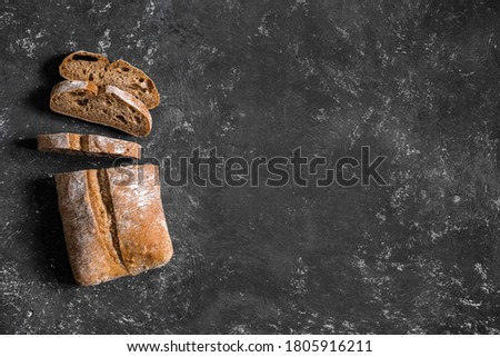 Ciabatta. Dark fresh healthy flattish open-textured Italian bread with a floury crust made with olive oil on black rustic background. Close-up. Top view Royalty-Free Stock Photo #1805916211