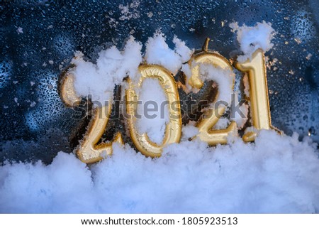 Candles in the form of numbers 2021 on a blue window glass background with snow and waterdrops. New Year celebration greeting card.