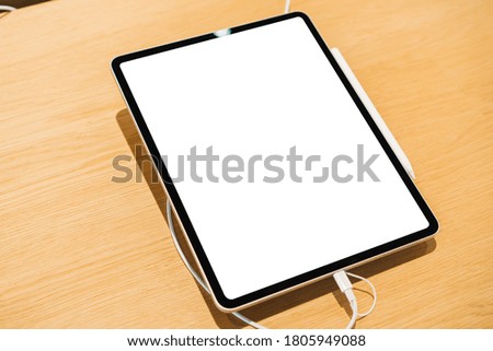 From above of modern tablet with blank screen and charging power bank placed on wooden table in light modern shop