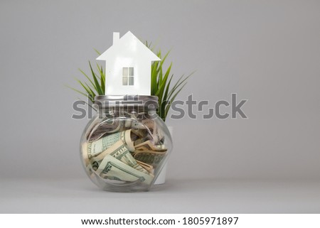 Glass piggy bank with dollars and on a gray background. Money set aside to rent and purchase of a house