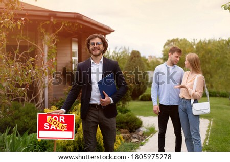 Confident realtor and happy young couple near beautiful country house outdoors
